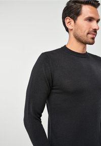 Suéter negro de manga larga hecho de un tejido de punto texturizado, con un cuello redondo acanalado y una silueta ajustada, sin patrones ni acentos visibles.