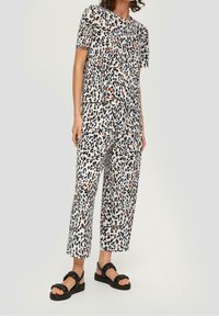 Dvoudílný outfit s leopardím potiskem, krátký rukáv, volný střih, odpovídající kalhoty, lehký materiál, černé akcenty a otevřené černé sandály.