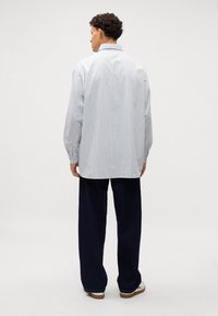 Camisa de manga larga a rayas en blanco y azul, con un corte relajado, cuello collado y detalles de botones. Combinada con pantalones sueltos de color azul marino.