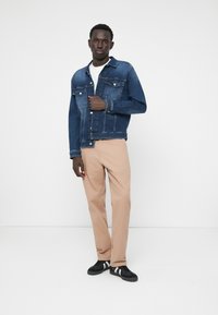 Tmavomodrá denimová bunda s prednými vreckami v kombinácii s khaki nohavicami. Čierne tenisky s bielymi akcentmi dopĺňajú celý outfit.