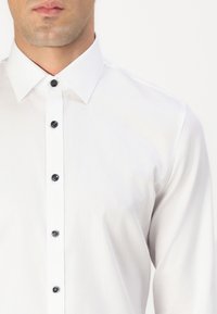 Hvit skjorte med knappestilling i teksturert stoff, klassisk krage og svarte knapper. Enkel design med moderne passform.