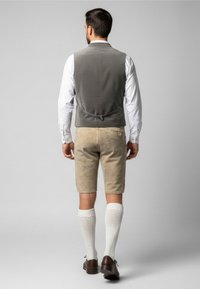 Šedá vesta přes bílé tričko, doplněná béžovými šortkami a bílými ponožkami do výšky kolen. Hnědé boty doplňují tradiční outfit.