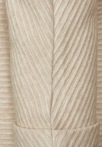 Beżowa tkanina z teksturowanym, prążkowanym wzorem. Projekt zawiera bezszwowy szew oraz małą, funkcjonalną kieszonkę na dole.