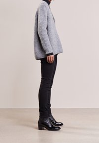 Maglione grigio a maglia oversize con texture a coste, abbinato a pantaloni neri slim-fit e stivaletti neri con tacco. Design minimalista.
