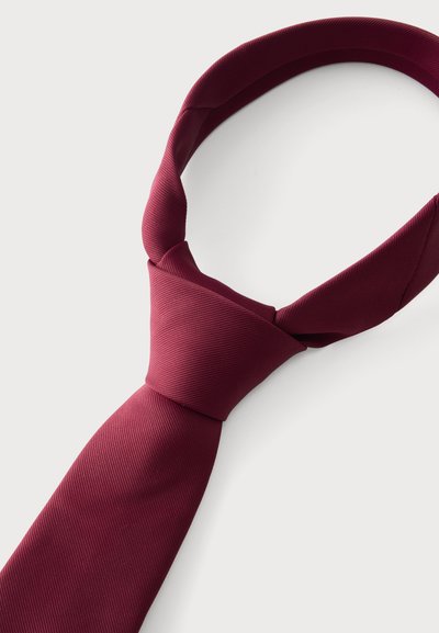 Cravate en soie rouge foncé nouée en un nœud classique sur un fond clair uni.