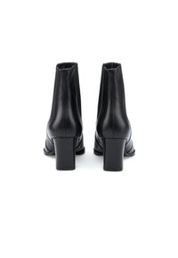 Bottines en cuir noir à texture lisse, bout arrondi, talon carré et silhouette ajustée. Conçues sans fermetures visibles.