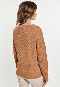 Brązowy sweter dziany z wzorem w romby, z prążkowanymi mankietami i dołem. Projekt jest lekki, o luźnym kroju i otwartej teksturze. 