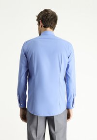 Camisa de manga larga en tela azul claro con cuello puntiagudo, puños con botón y dobladillo recto, que presenta una textura suave y un ajuste entallado.