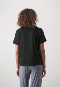 Melnas kokvilnas T-kreklis ar īsām piedurknēm, ar brīvu piegriezumu un apli apkaklī. Mugurpuses skats parāda gludu tekstūru un vienkāršu dizainu.