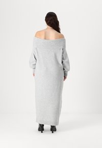 Sivo oblačilo z dolgimi rokavi in odkrito rameno, z rebrastim ovratnikom in manšetami, izdelano iz mehkega pletenega materiala, do kolen, v kombinaciji s črnimi petkami.
