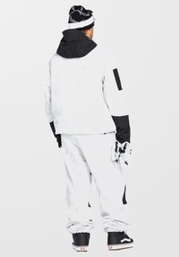 Snowboardoutfit bestående af en hvid og sort vandtæt jakke med lommer, matchende hvide bukser og sorte sko. Huens mønster er sort og hvidt.