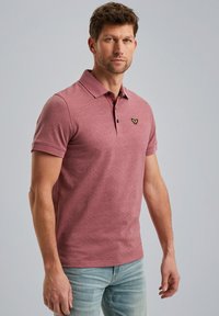 Polo rose à motifs avec un col, des manches courtes et un petit logo noir sur la poitrine. Porté avec un jean bleu clair.