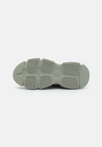 Suola di una sneaker in gomma verde chiaro, con evidenti modelli di battistrada e sezioni sagomate per la trazione. Finitura liscia.