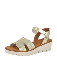 Sandalias de cuña de color dorado claro con diseño de tiras cruzadas, textura perforada y hebilla ajustable en el tobillo. Suela de plataforma color crema con ranuras.