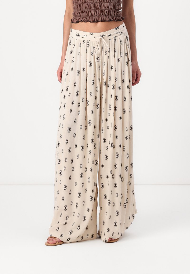 Pantalons larges de couleur crème avec un motif abstrait de losanges noirs. Dotés d'une taille à cordon de serrage et d'un tissu léger et texturé.