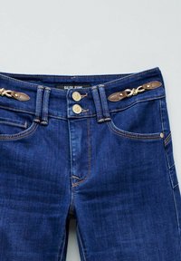 Jeans de mezclilla azul oscuro con una cintura alta, cierres de botón dorado y detalles en cuero marrón en la cintura. Presenta bolsillos delanteros y detalles de costura.