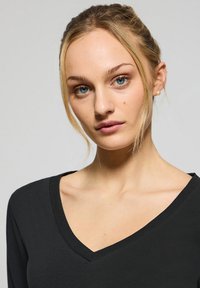 Svart långärmad topp med V-ringning, gjord av ett mjukt tyg med en enkel, ren skärning. Minimalistisk stil utan utsmyckningar.