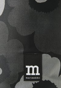 Black textile featuring large grey floral patterns, with a woven label displaying the letter "m" and the brand name "marimekko."