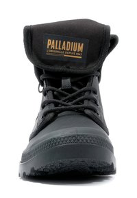 Încălțăminte din cauciuc negru, cu un design robust, șireturi texturate și un vârf din pânză pliabil. Include o etichetă cu logo pe limba încălțămintei.