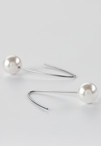 Pendientes de gota de perlas con un brillante alambre metálico plateado. Las perlas son esféricas, lisas y blancas, realzando el diseño minimalista.