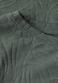 Tela de camiseta en verde oscuro con un patrón texturizado de hojas, con un escote redondo y material de punto suave y liso.