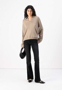 Maglione oversize beige a maglia con colletto, abbinato a jeans neri a zampa. Borsa nera e scarpe slip-on con dettagli circolari.