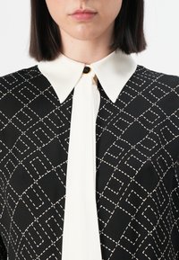 Black patterned blouse featuring a white collar, with a geometric design and button detail at the neck. Smooth fabric texture, tailored fit.