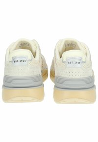 Helle Sneaker mit einem strukturierten, weichen Obermaterial, grauen Akzenten und einer Gummisohle. Merkmale sind ein Anhänger mit "EST. 1949" an der Ferse.