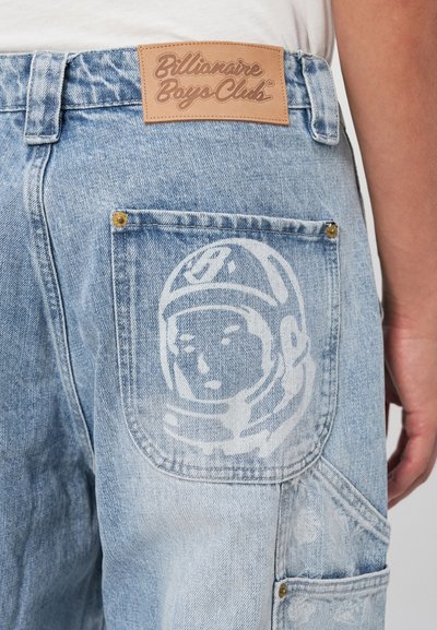 Pantalones cargo de mezclilla en azul claro con un gráfico visible de un astronauta en el bolsillo trasero, que cuenta con un parche de cuero de la marca y costuras en contraste.