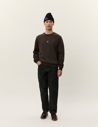 Felpa marrone con un piccolo design bianco "II", abbinata a jeans scuri e scarpe nere. Il modello indossa un berretto nero.
