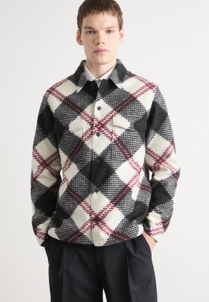 Plaid flannel shirt in cream, black, and red, featuring a button-front, two chest pockets, and a collared neck design. Soft texture.