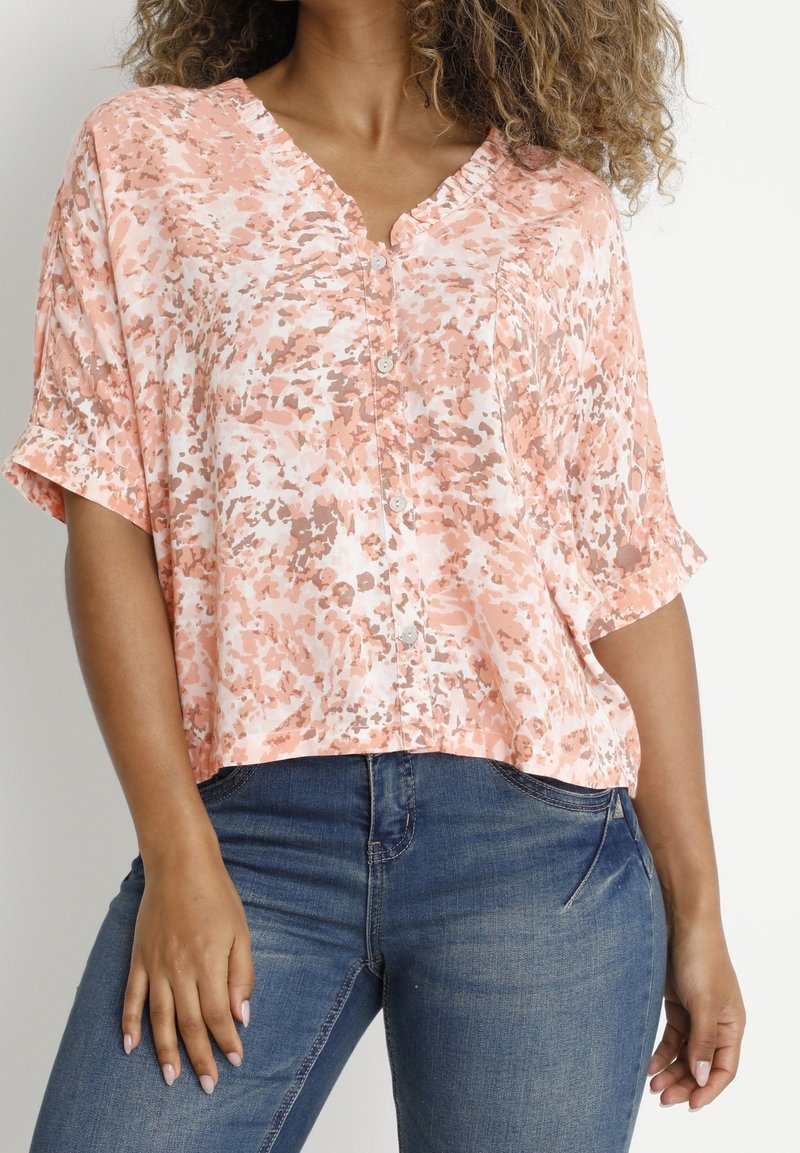 Blusa a maniche corte, con bottoni, realizzata in tessuto morbido e leggero, con un motivo astratto rosa e beige. Design a V e vestibilità rilassata.