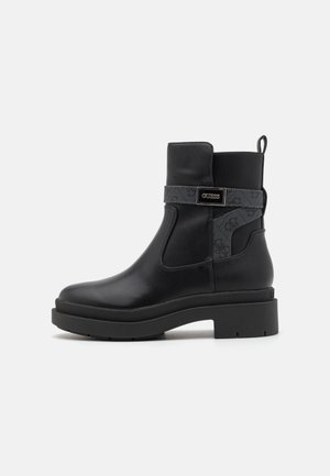 Bottes en cuir noir à la cheville avec une semelle épaisse, dotées d'une sangle en tissu décorative et d'un accent logo sur le côté. Détail de panneau texturé.