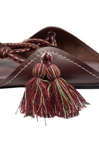 Brązowe skórzane sandały o teksturowanym wykończeniu, dekoracyjne frędzle w kolorze czerwonym i zielonym oraz szeroki w nosie design z detalami przeszycia.