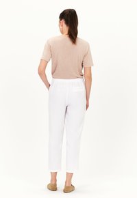 T-shirt beige chiaro a maniche corte abbinato a pantaloni di lino bianchi con vita elasticizzata e tasca posteriore.