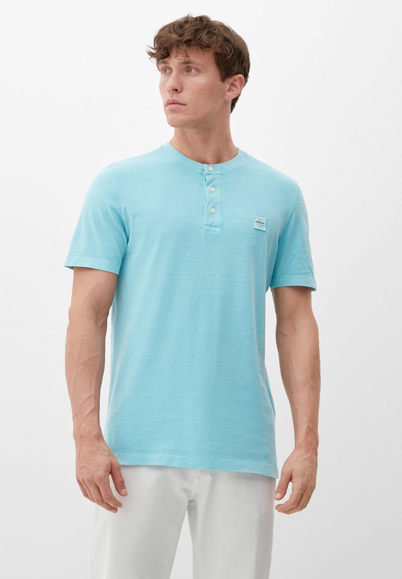 Svetlo modra kratka majica henley z mehkim materialom, ki vključuje tri gumbe na izrezu in majhno oznako logotipa na prsih.