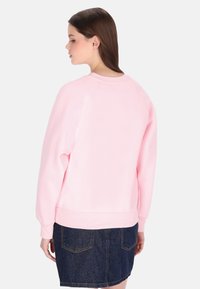 Lichtroze sweatshirt van zacht materiaal, met een klassieke ronde hals en geribde manchetten, gecombineerd met een donkere denim rok.