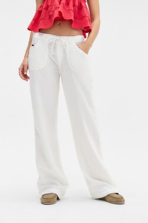 Pantalons blancs à jambes larges en tissu texturé. Dotés d'une taille à cordon de serrage et de deux grandes poches avant. Portés avec des chaussures marron à enfiler.