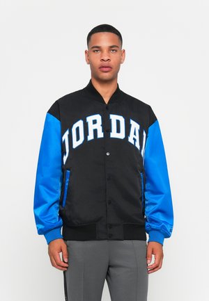 Black and blue varsity jacket featuring bold white "JORDAN" lettering, a snap-button front, and ribbed cuffs. Smooth fabric with side pockets.