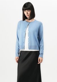 Lyseblå cardigan laget av mykt materiale, med rund halsutskjæring, fullt lengde armer og knappeåpning foran.