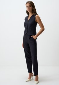 Navy pinstriped vest en tapse broekset met een V-hals, knoopsluiting en zijzakken. Gecombineerd met witte hoge hakken.