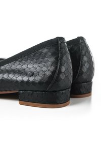 Ballerine nere con tomaia in pelle a squame testurizzata e tacco basso quadrato. I bordi sono rifiniti con un morbido e elastico bordo.