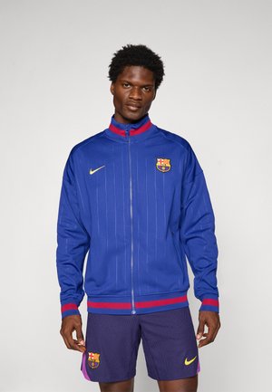 Blue zip-up track jacket with pinstripes, red and blue ribbed collar and cuffs, Nike logo, and FC Barcelona crest on the chest.