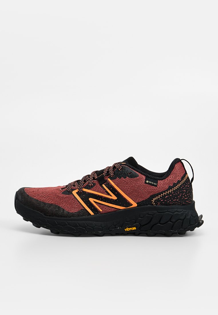 Zapatilla de trail running en rojo y negro con logo naranja "N", suela negra Vibram, etiqueta Gore-Tex y detalle de patrón en el talón, vista lateral sobre fondo blanco.