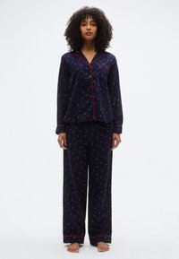 Ensemble de pyjama bleu marine avec passepoil rouge ; le haut présente un design boutonné et des manches longues, tandis que le pantalon est ample avec un motif floral.