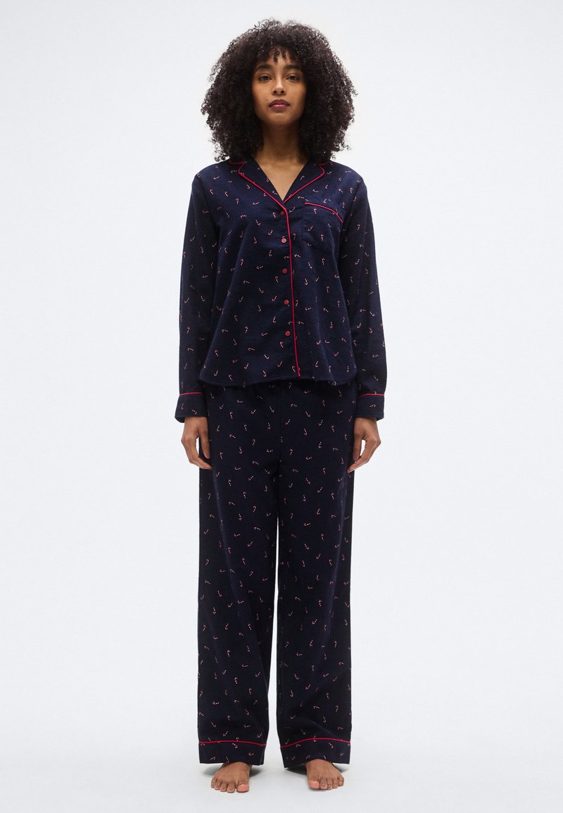Ensemble de pyjama bleu marine avec passepoil rouge ; le haut présente un design boutonné et des manches longues, tandis que le pantalon est ample avec un motif floral.