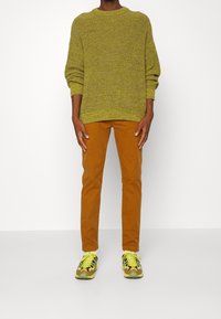Pull vert tricoté, pantalon orange-brun et baskets multicolores avec des accents jaunes. Coupe décontractée, poignets côtelés et tissu texturé.
