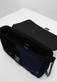 Tmavě modré sametové psaníčko s květinovou výšivkou, stříbrnými kovovými detaily a řetízkovým popruhem. Vnitřek je podšitý černou látkou a obsahuje kapsu na zip.