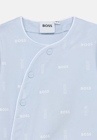 Βρεφικό φορμάκι σε ανοιχτό μπλε χρώμα, κατασκευασμένο από απαλό ύφασμα, με επαναλαμβανόμενο λευκό κείμενο "BOSS", κουμπιά τύπου snap και στρογγυλή λαιμόκοψη.