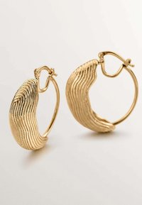 Pendientes de oro en forma de aro con un diseño texturizado y ondulado. Cuentan con un cierre de bisagra y un acabado pulido, creando un aspecto elegante y contemporáneo.